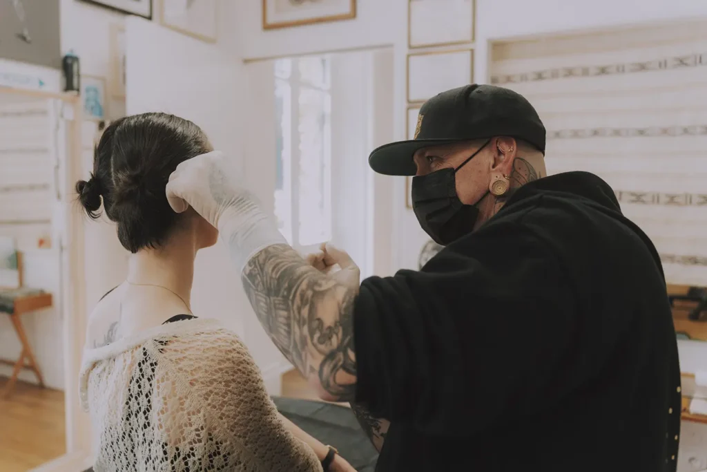 Consultation : Le perceur Ernest examine l'oreille d'une cliente pour le placement d'un bijou Buddha Jewelry chez Vauban à Bayonne, capturé par l'agence ADIO.