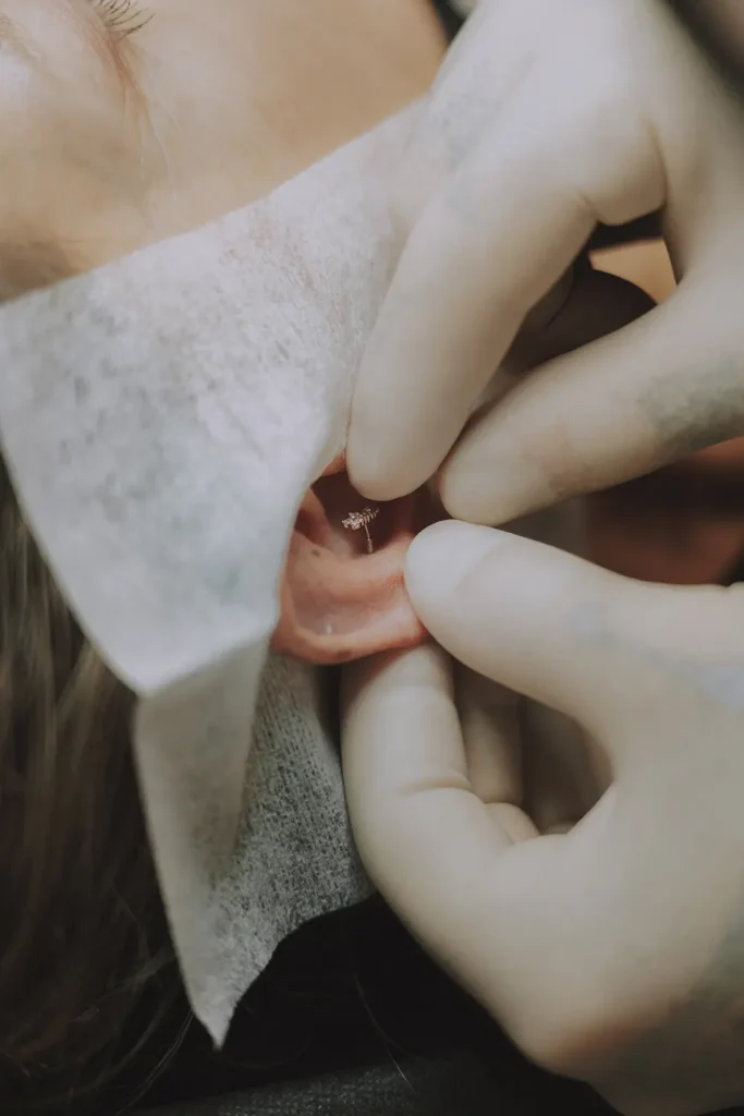Détail technique : Vue macro sur l'insertion délicate d'un bijou de cartilage par un expert chez Vauban Piercing à Bayonne, photo par l'agence ADIO.