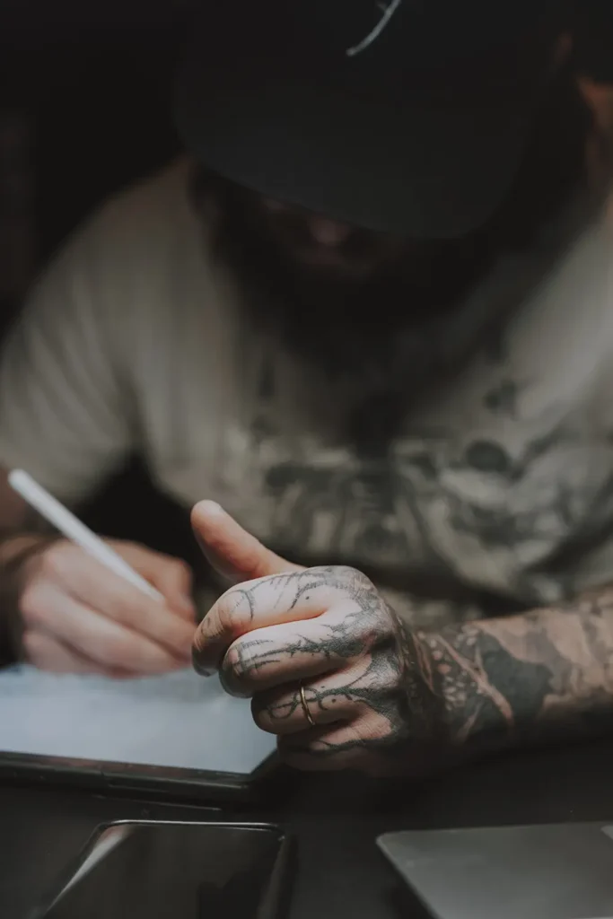 Photo de détail : Gros plan sur la main tatouée de l'artiste peaufinant un croquis chez Hamsaran Tattoo à Bayonne, par l'agence ADIO.