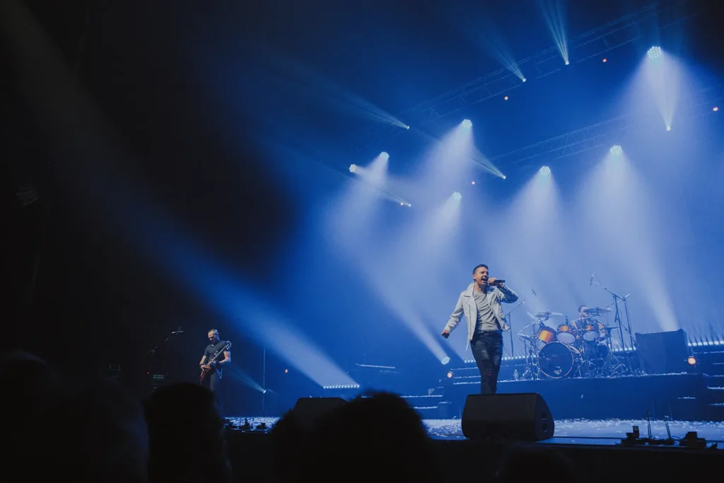 Concert : chanteur en blanc sous des projecteurs bleus à l'Arkéa Arena par l'agence ADIO