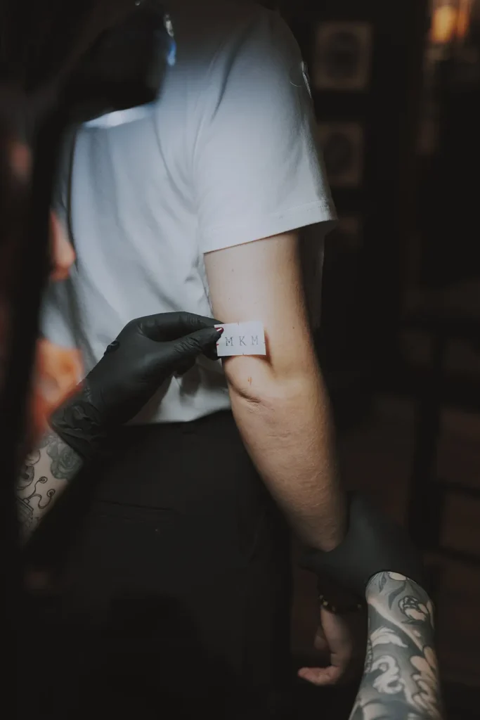 Photographie de détail : Pose précise d'un stencil sur le bras d'un client au shop Hamsaran Tattoo à Bayonne, par l'agence ADIO.