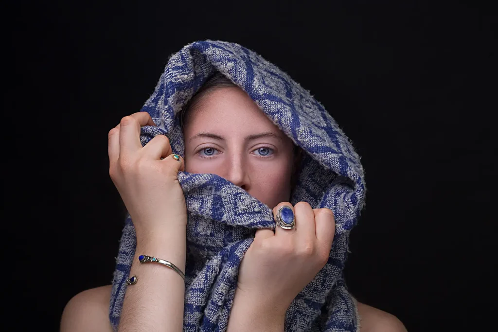 Portrait serré visage avec écharpe, yeux bleus et détails bijoux sur fond noir par Studio Adio.