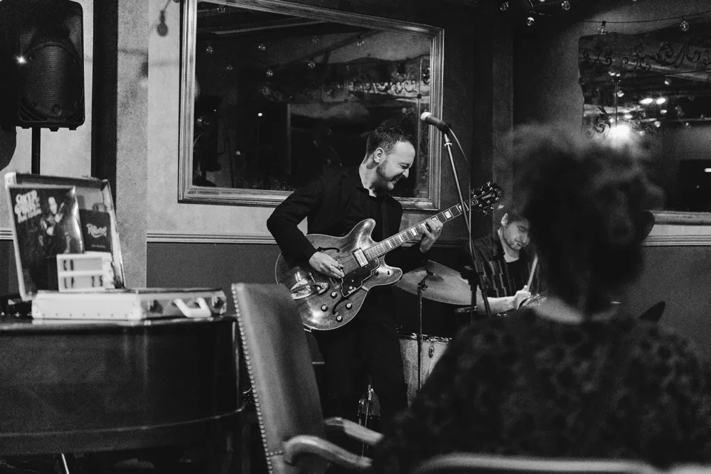 Reportage photo : guitariste jazz souriant jouant sur scène au Prohibido Jazz Club, image réalisée à Biarritz par l'agence ADIO.