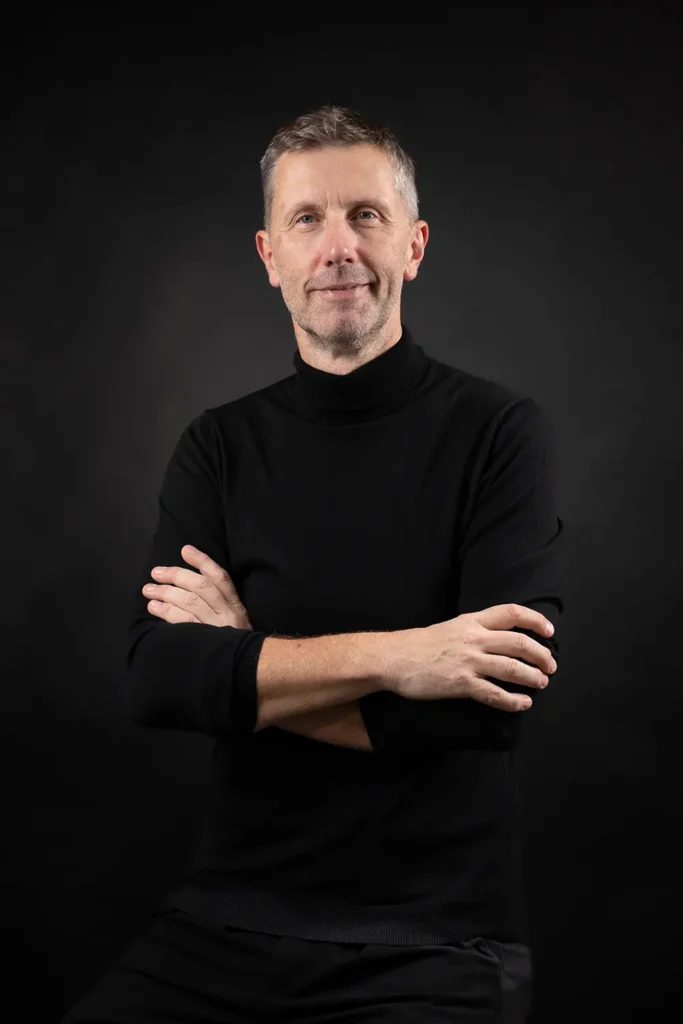 Shooting photo : portrait élégant et souriant de Yves Bouillier, bras croisés sur fond sombre par l'agence ADIO.