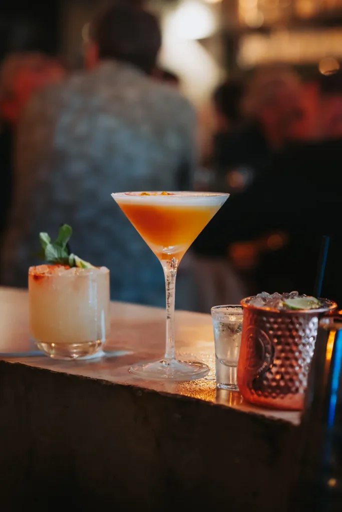 Mise en avant : Alignement de trois cocktails colorés sur le comptoir du bar Kubata à Bayonne, réalisé par l’agence ADIO