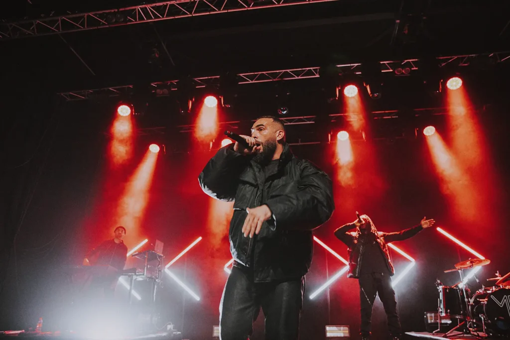 Photographie live : Médine et ses musiciens en pleine performance sous un éclairage rouge intense à l'Atabal par l'agence ADIO