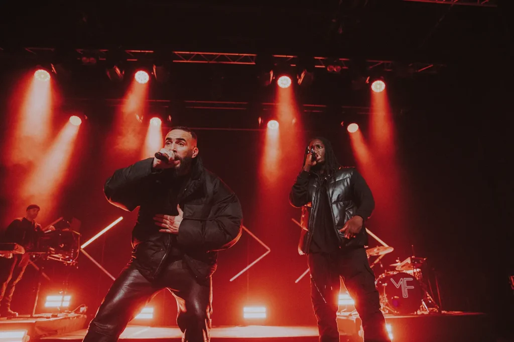 Reportage photo concert : Médine et son backeur chantant sous un éclairage rouge intense à l'Atabal Biarritz capturés par l'agence ADIO