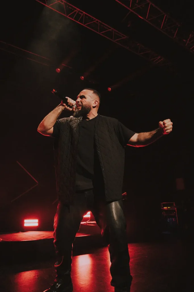 Mise en valeur artiste : Portrait en pied de Médine chantant avec puissance sous une lumière rouge sombre à l'Atabal par l'agence ADIO