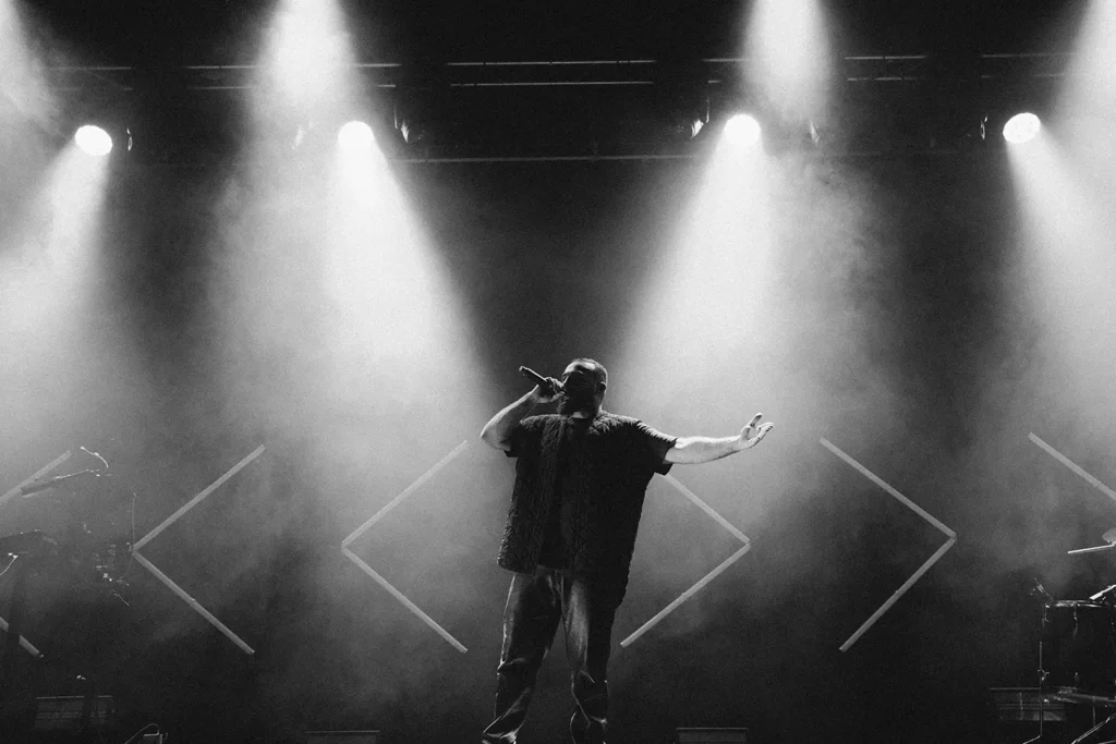Mise en avant artiste : Médine seul sur scène les bras ouverts dans un faisceau de lumière brumeux à l'Atabal par l'agence ADIO