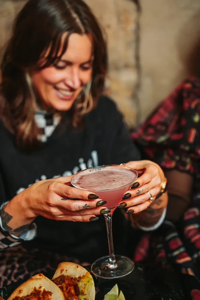 Portrait mood : Cliente souriante tenant un cocktail rose dans l'ambiance du Kubata à Bayonne, par l’agence ADIO