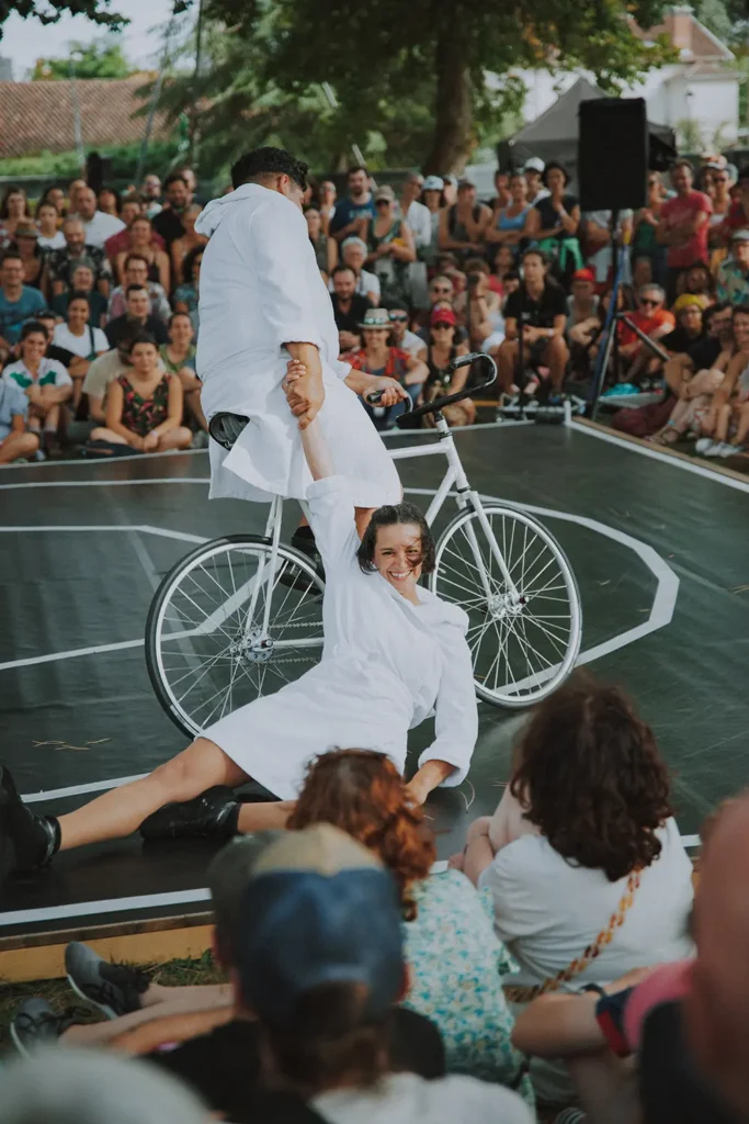 Reportage arts du cirque : duo d'acrobates en peignoirs blancs sur un vélo au festival Musicalarue par l'agence ADIO